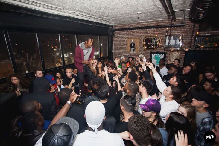 Rapper Travis Scott stands on a table while working a huge crowd at Apt 200
