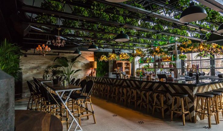 L’intérieur du jardin de Kampai avec un grand bar est avec beaucoup de plantes et de luminaires industriels. Bon spot enterrement de vie de garçon à Montréal