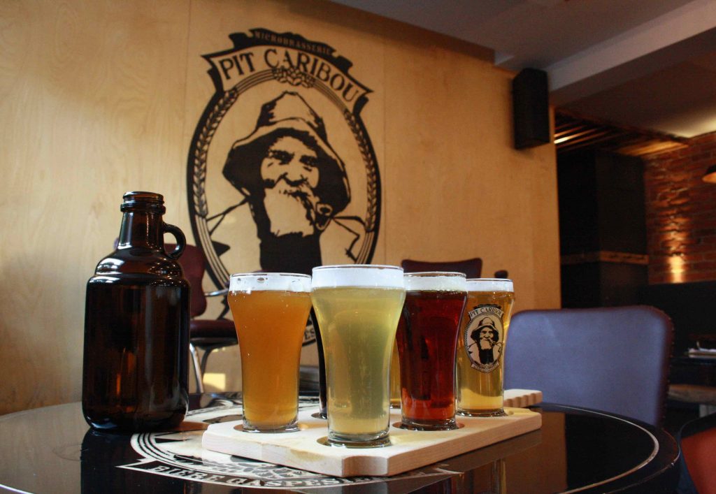 arrangement of four beers on a table in front of Pit Caribou logo on wall - best brewpubs in montreal
